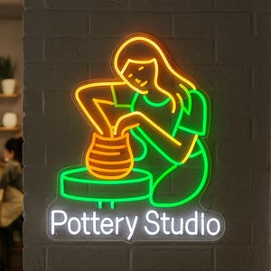 May include: Neon sign for a pottery studio. The sign depicts a person working on a pottery wheel, with the words "Pottery Studio" below. The sign is outlined in green and orange, with a white border.