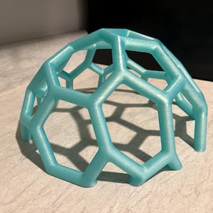 May include: A light blue, 3D-printed geometric dome with a honeycomb-like structure. The object is made of plastic and has a smooth, slightly shiny surface. The dome is approximately 4 inches wide and 3 inches tall.