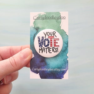 May include: A white button with a red, white, and blue American flag design and the text "YOUR VOTE MATTERS!" on a white card with blue and green watercolor background. The card also includes the text "Carlydoodleydoo.etsy.com".