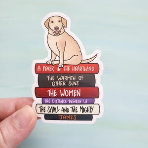 May include: A sticker of a yellow Labrador Retriever sitting on a stack of books. The books have the titles "A Fever in the Heartland", "The Warmth of Other Suns", "The Women", "The Distance Between Us", "The Small and the Mighty", and "James".