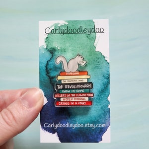 May include: A stack of books with a squirrel reading on top. The book titles are "Homegoing", "The Righteous Mind", "The Revolutionary", "Know My Name", "Killers of the Flower Moon", "Hidden Potential", and "Crying in H-Mart".