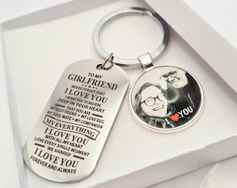 May include: A silver keychain set inside a white gift box. The keychain includes a dog tag with engraved text and a round charm with a photo. The dog tag reads "TO MY GIRLFRIEND I LOVE YOU" and other loving phrases. The round charm has a photo of a person.