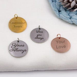 Op de afbeelding: Vier ronde metalen hangers in goud, zilver en roségoud. Elke hanger heeft een kleine lus aan de bovenkant. De hangers zijn gegraveerd met de zinnen "Customise Yours", "Love you always", "Yours Always" en "Your Love".