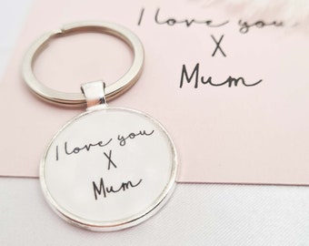 May include: A silver keychain with a round glass charm that says "I love you X Mum" in black handwriting. The keychain is on a pink card with the same message written in black handwriting.