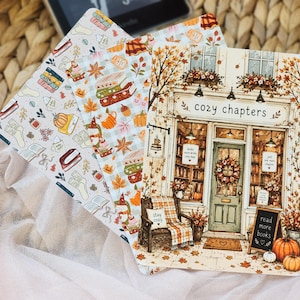 May include: Three rectangular bookmarks featuring autumn-themed illustrations. One shows a bookstore storefront labeled 'cozy chapters' with a 'read more books' sign, while the others display patterns of books, pumpkins, leaves, and mugs.