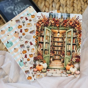 May include: Three rectangular bookmarks featuring autumn themes. One displays a light blue plaid pattern with orange and green pumpkins. Another shows a cream background with small icons of books, mugs, and leaves. The third depicts a library entrance.