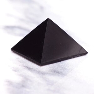 May include: A black obsidian pyramid crystal, a smooth, polished, geometric shape with four triangular sides and a pointed top.