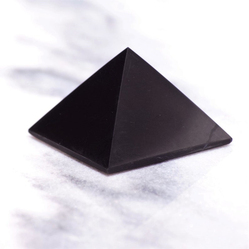 May include: A black obsidian pyramid crystal, a smooth, polished, geometric shape with four triangular sides and a pointed top.