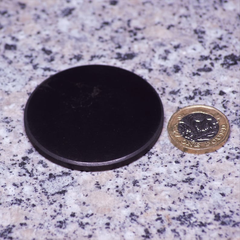 May include: A black round disc next to a gold British one pound coin. The coin has the inscription "One Pound" and a depiction of a royal figure.