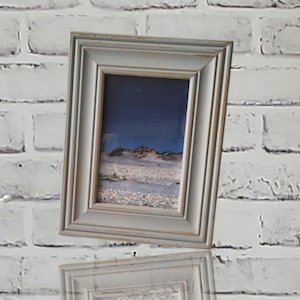 May include: A gray picture frame with a distressed finish. The frame is holding a photograph of a beach scene with a blue sky and white sand.