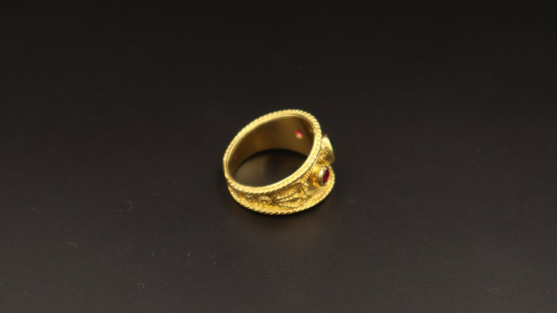 May include: A gold ring with intricate detailing and two red gemstones.