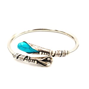 May include: A silver bangle bracelet with an ornate design and a turquoise stone accent.