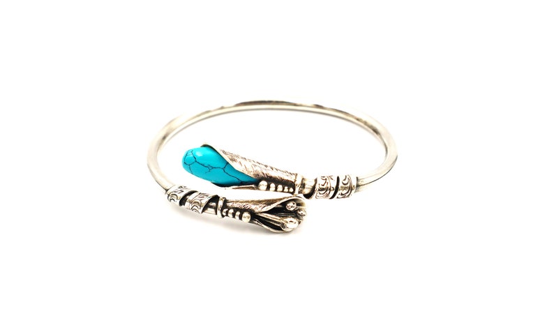 May include: A silver bangle bracelet with an ornate design and a turquoise stone accent.