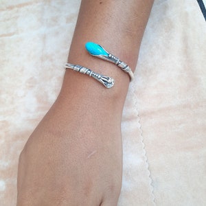 May include: A silver bracelet with a turquoise stone on the end. The bracelet is in the shape of a snake.