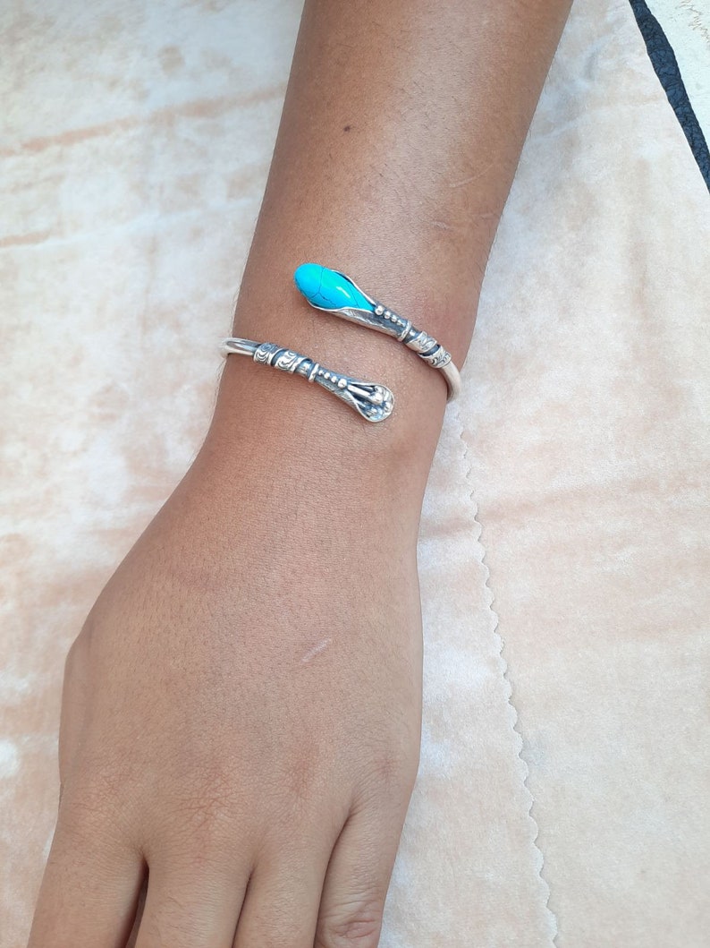 May include: A silver bracelet with a turquoise stone on the end. The bracelet is in the shape of a snake.