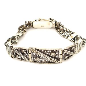Puede incluir: Un brazalete de plata con intrincados dise&ntilde;os de filigrana y peque&ntilde;as piedras transparentes. El brazalete tiene un dise&ntilde;o de cadena doble y un cierre.