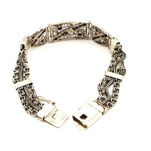 Puede incluir: Un brazalete de plata con un dise&ntilde;o delicado e intrincado. El brazalete est&aacute; hecho de m&uacute;ltiples hebras de cadena que est&aacute;n entrelazadas. El cierre es una simple barra de plata.