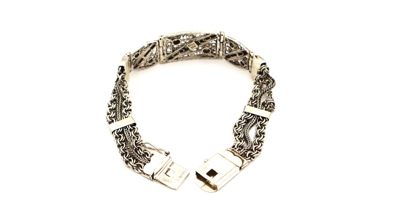 Puede incluir: Un brazalete de plata con un dise&ntilde;o delicado e intrincado. El brazalete est&aacute; hecho de m&uacute;ltiples hebras de cadena que est&aacute;n entrelazadas. El cierre es una simple barra de plata.