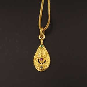 Op de afbeelding: Een gouden ketting met een hanger in de vorm van een traan. De hanger is versierd met drie edelstenen: een roze steen in het midden en twee groene stenen aan weerszijden.