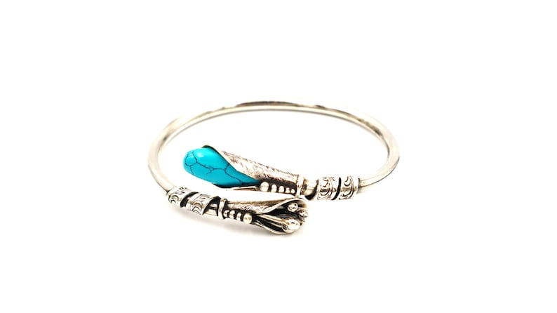 May include: A silver bangle bracelet with an ornate design and a turquoise stone accent.