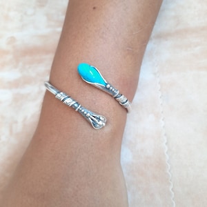May include: A silver bracelet with a turquoise stone. The bracelet is shaped like a snake with a curled tail.
