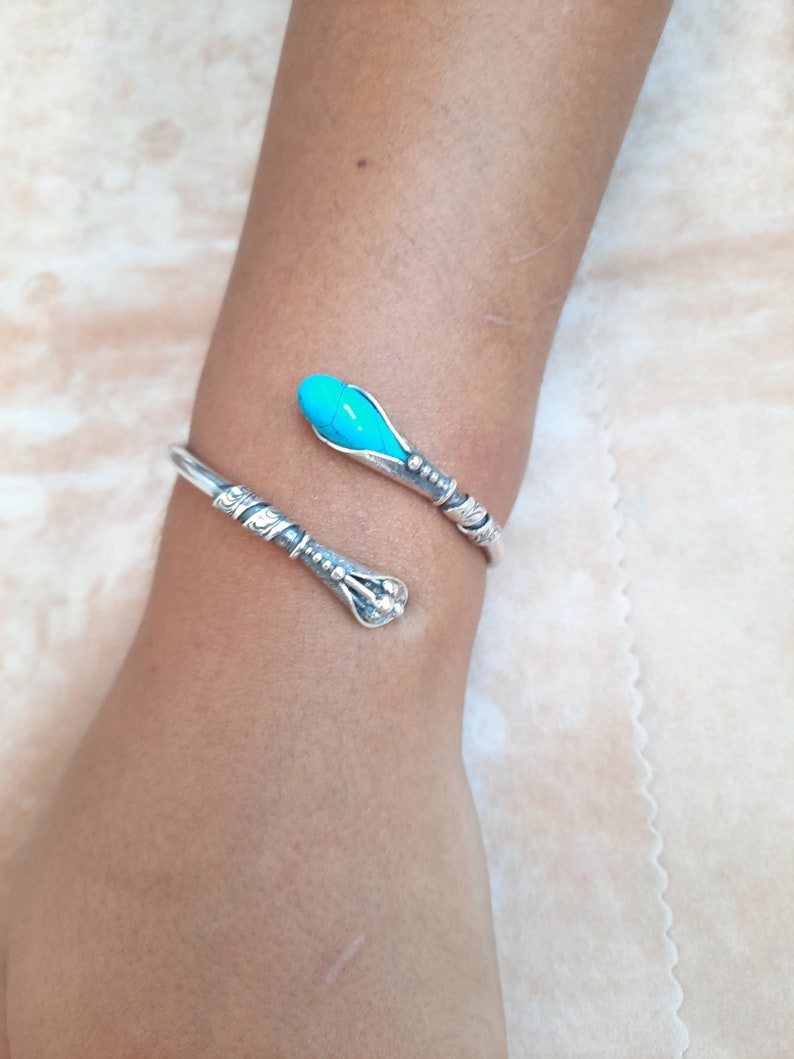 May include: A silver bracelet with a turquoise stone. The bracelet is shaped like a snake with a curled tail.