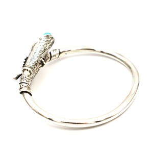 May include: A silver bracelet with a detailed design featuring a turquoise stone. The bracelet is open and has a circular shape.