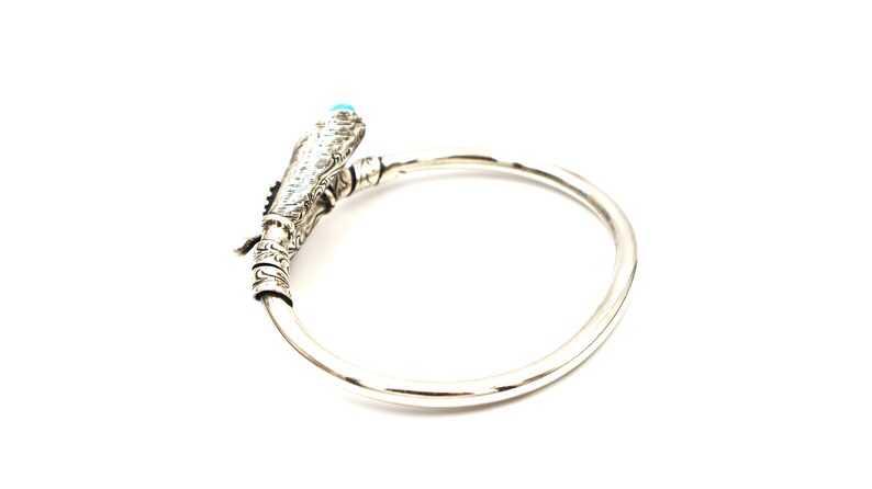 May include: A silver bracelet with a detailed design featuring a turquoise stone. The bracelet is open and has a circular shape.