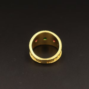 May include: Gold ring with three small gemstones, one green and two red, set into the band.