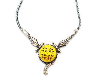 Puede incluir: Un collar de cadena de plata con un colgante amarillo tallado con un diseño floral. El colgante está acentuado con un pequeño diamante.