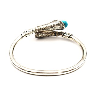 May include: Silver bangle bracelet with a turquoise stone and an intricate design. The bracelet is open and has a snake-like design.