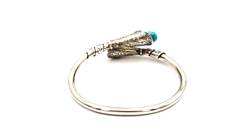 May include: Silver bangle bracelet with a turquoise stone and an intricate design. The bracelet is open and has a snake-like design.