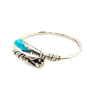 May include: Silver bangle bracelet with a turquoise stone and intricate detailing.