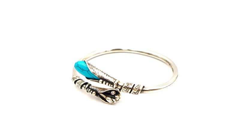 May include: Silver bangle bracelet with a turquoise stone and intricate detailing.