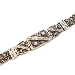 Puede incluir: Un brazalete de plata con un dise&ntilde;o de cadena de eslabones y detalles rectangulares decorativos. Los detalles presentan un patr&oacute;n geom&eacute;trico y peque&ntilde;as piedras transparentes.