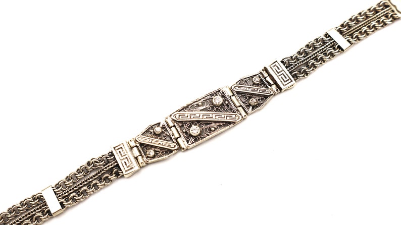 Puede incluir: Un brazalete de plata con un dise&ntilde;o de cadena de eslabones y detalles rectangulares decorativos. Los detalles presentan un patr&oacute;n geom&eacute;trico y peque&ntilde;as piedras transparentes.