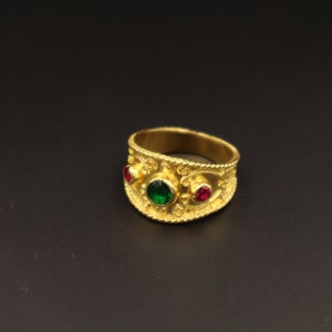 May include: A gold ring with a green and two red gemstones set in an ornate band.