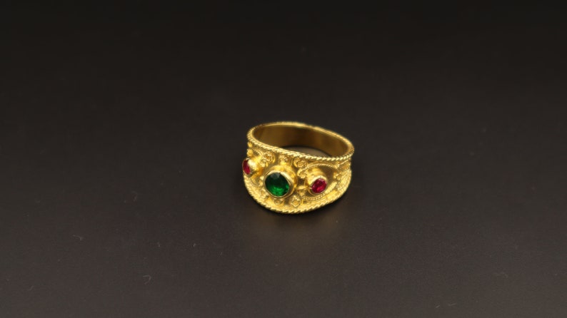 May include: A gold ring with a green and two red gemstones set in an ornate band.