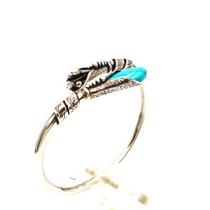 May include: Silver bangle bracelet with a turquoise stone and intricate silver detailing.