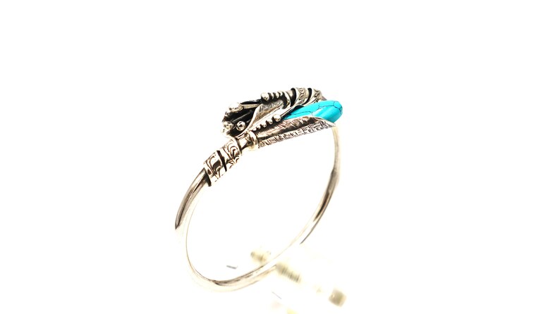 May include: Silver bangle bracelet with a turquoise stone and intricate silver detailing.