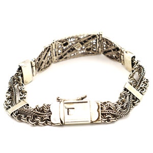 Puede incluir: Un brazalete de plata con un dise&ntilde;o de filigrana y un cierre de broche.