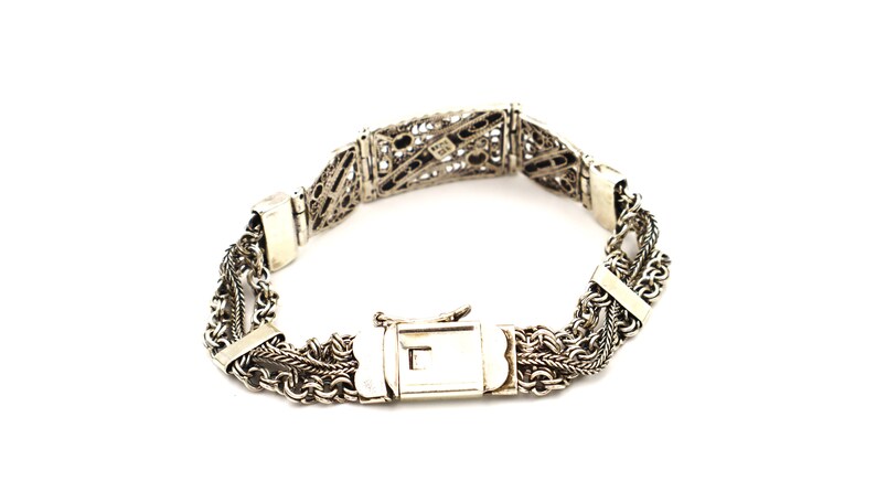 Puede incluir: Un brazalete de plata con un dise&ntilde;o de filigrana y un cierre de broche.