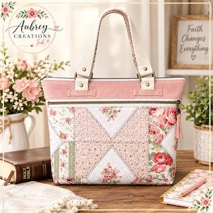 May include: A tote bag featuring a patchwork design of pink and white floral patterns, a solid pink upper panel, and cream-colored fabric handles. The bag includes a horizontal zippered pocket on the front with a pink tassel pull and metal hardware.