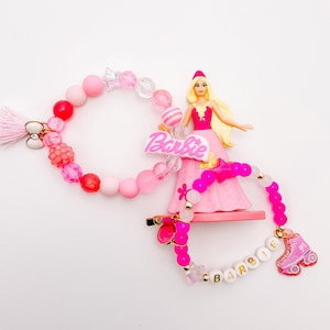 Puede incluir: Pulseras de cuentas rosas y blancas con un dije de Barbie rosa y un dije de patines rosa. Las pulseras deletrean "Barbie" y "Barbie".