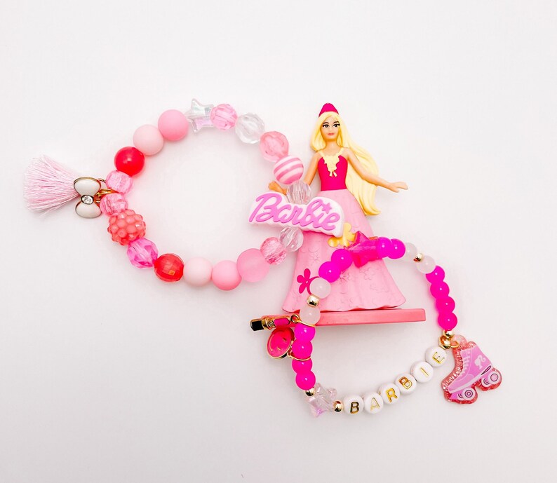 Puede incluir: Pulseras de cuentas rosas y blancas con un dije de Barbie rosa y un dije de patines rosa. Las pulseras deletrean "Barbie" y "Barbie".