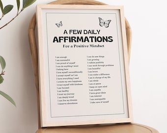 Könnte beinhalten: Ein gerahmter Druck mit einem hellen Holzrahmen und weißem Hintergrund. Der Druck zeigt eine Liste täglicher Affirmationen für eine positive Denkweise mit dem Titel "A Few Daily Affirmations For a Positive Mindset". Der Druck ist mit zwei kleinen Schmetterlings-Illustrationen verziert.