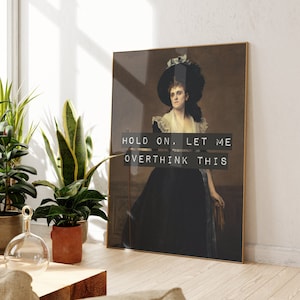 May include: A framed print of a woman in a black dress and a large hat. The text "HOLD ON, LET ME OVERTHINK THIS" is printed in white on a black background.