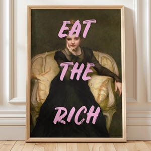 Könnte beinhalten: Ein gerahmter Kunstdruck mit einem Porträt einer Frau in einem schwarzen Kleid, die in einem vergoldeten Stuhl sitzt. Die Worte "EAT THE RICH" sind in rosa, stilisiertem Text über das Bild gelegt.