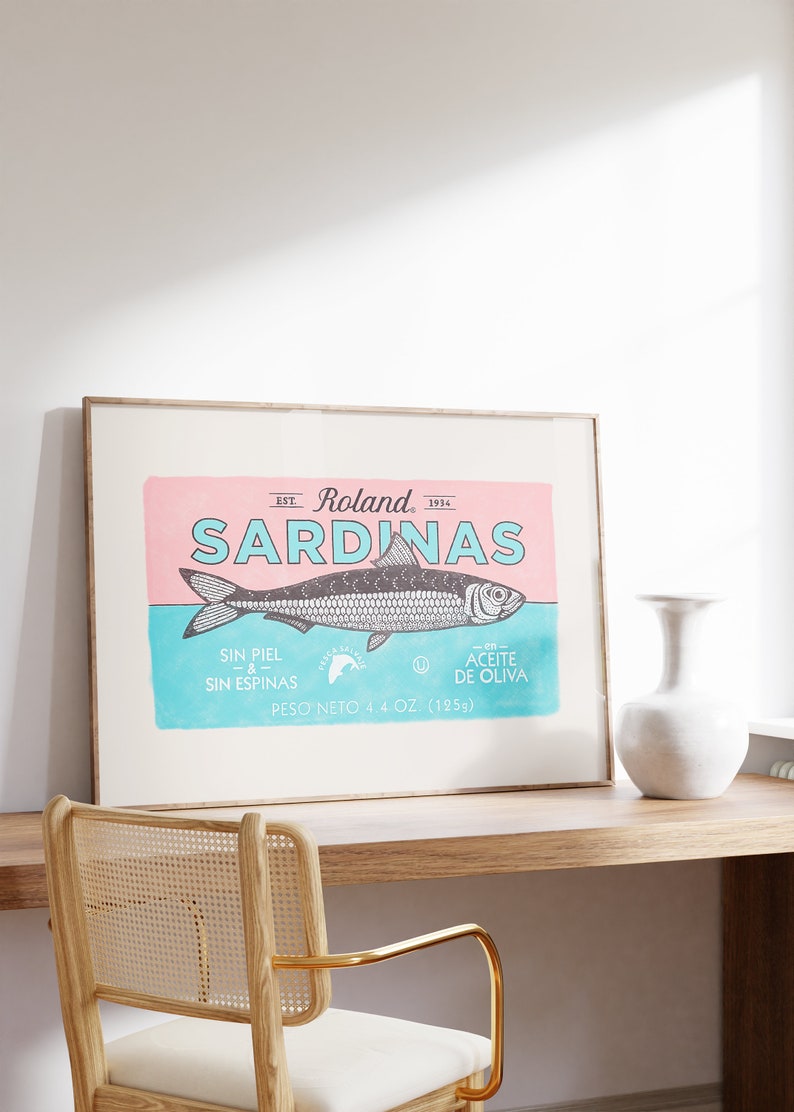 May include: A framed vintage-style poster with a pink and blue background featuring a sardine illustration and the text "EST. Roland, 1934 SARDINAS SIN PIEL -&- SIN ESPINAS 0 -en- ACEITE DE OLIVA PESO NETO 4.4 OZ. (125g)"