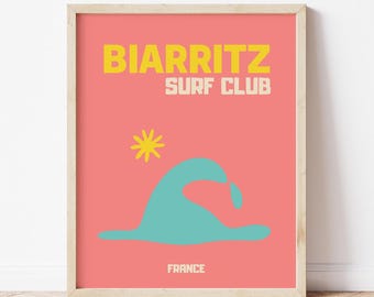 Puede incluir: Un póster enmarcado con un fondo de color salmón. El póster presenta las palabras "BIARRITZ SURF CLUB" en amarillo y blanco, una ilustración de ola turquesa, una estrella amarilla y la palabra "FRANCE" en blanco.